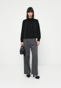 Top nero a maniche lunghe con collo alto, abbinato a pantaloni grigi a gamba larga. Gli accessori includono una piccola borsa nera e scarpe col tacco nere.
