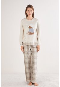 Suéter beige claro con un dibujo de oso con suéter azul; combinado con pantalones de franela beige y a cuadros en tela suave.