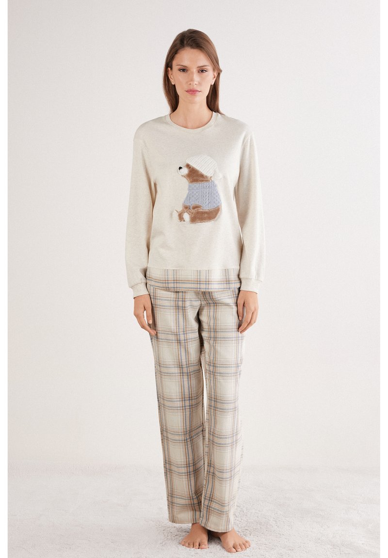 Suéter beige claro con un dibujo de oso con suéter azul; combinado con pantalones de franela beige y a cuadros en tela suave.