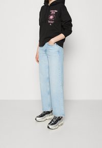 Svart hoodie med rosa grafisk text, ljusblå vida jeans och svarta och metalliska sneakers. Har en avslappnad passform och fickor.