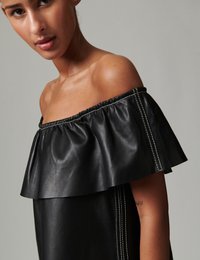 Μαύρο δερμάτινο τοπ με ανοικτούς ώμους, φαρδιά ρεβέρ διακοσμημένα με βολάν και αντίθετη λευκή ραφή. Ομαλή υφή και άνετη εφαρμογή.