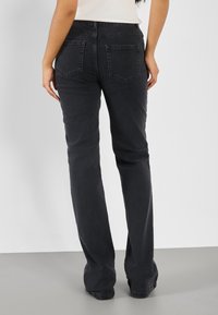 Schwarze Jeans im geraden Schnitt, ausgestattet mit zwei Gesäßtaschen und einem Bund. Der Stoff hat eine glatte, robuste Textur.