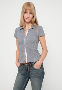 Camisa de manga curta com padrão vichy azul-marinho e branco, com gola com acabamento em renda e corte ajustado. Combinada com jeans.