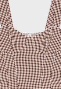 Haut sans manches à motif vichy marron et blanc, col carré et détails froncés au niveau de la poitrine.