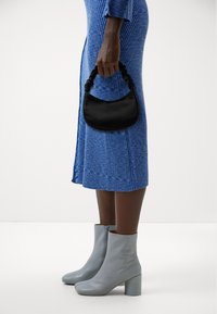 Black handbag with a gathered handle, worn with a blue ribbed dress and light gray ankle boots with a block heel.