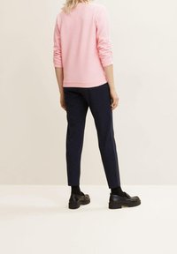 Rosa, texturerad sweatshirt med långa ärmar, i kombination med marinblå slim-fit byxor och svarta kraftiga skor. Enkel, minimalistisk design.