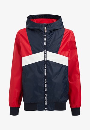 Chaqueta cortavientos con capucha, mangas rojas, cuerpo azul marino, franja blanca en forma de chevron y cremallera central con la etiqueta "8TH STREET."