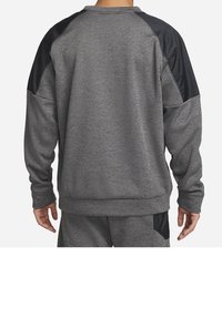 Homme portant un survêtement gris avec des accents noirs sur les épaules et les poches, vu de dos sur un fond uni.