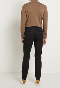 Brown turtleneck sweater, black slim-fit pants, and white sneakers with brown accents; casual attire viewed from behind.