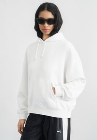 Ανοιχτό γκρι φούτερ με κουκούλα, μπροστινή τσέπη, κορδόνια και διακριτικό λογότυπο. Συνδυάζεται με μαύρο αθλητικό παντελόνι που έχει λευκή ρίγα και λογότυπο.