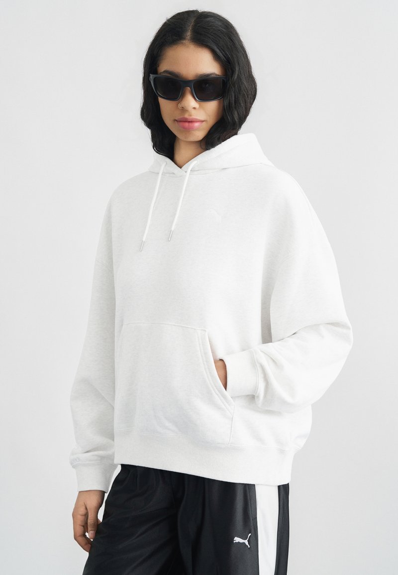 Ανοιχτό γκρι φούτερ με κουκούλα, μπροστινή τσέπη, κορδόνια και διακριτικό λογότυπο. Συνδυάζεται με μαύρο αθλητικό παντελόνι που έχει λευκή ρίγα και λογότυπο.