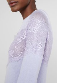 Maglione lilla con inserti in pizzo trasparente sulle spalle, texture liscia, design aderente e classico scollo a girocollo.