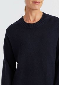 Navy-blauer Strickpullover mit einem gerippten Rundhalsausschnitt und lockerem Schnitt, langen Ärmeln und weicher Textur.