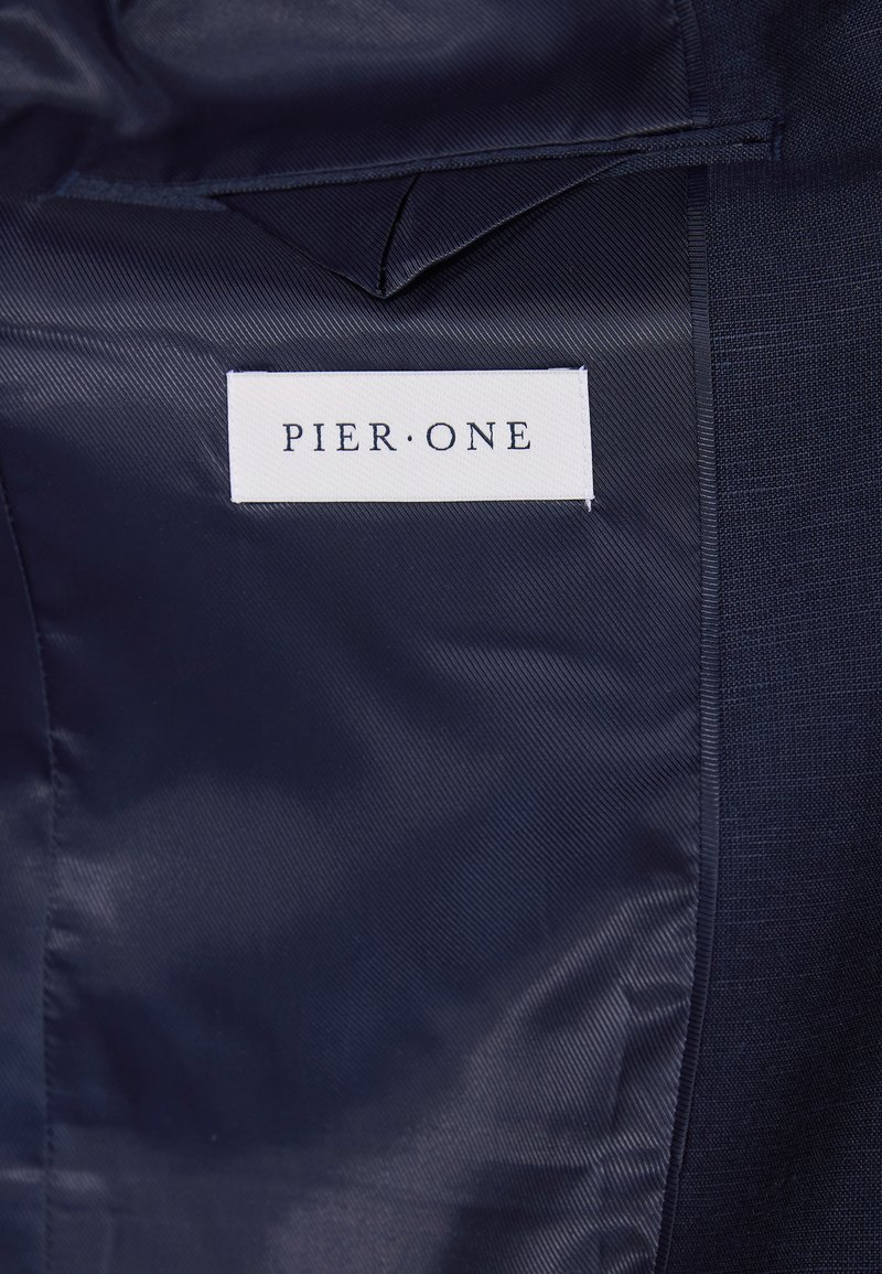 Tissu marine avec une texture lisse ; présente une étiquette blanche avec "PIER·ONE" en police noire. Deux types de tissus visibles, créant une dimension.