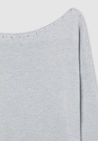 Maglione grigio lavorato a maglia con un design off-shoulder, caratterizzato da borchie argento lungo il collo per un tocco di dettaglio in più. Texture morbida e forma casual.