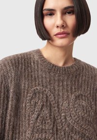 Brun strikket sweater med ribbet struktur og hævet swirl-mønster, med rund halsudskæring og blødt, fluffy materiale.