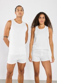 Två modeller bär vita, ribbade linnen och matchande shorts. Tygkvaliteten verkar lätt, med en mjuk textur och minimalt med detaljer.