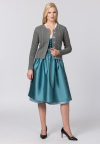 Graue Strickjacke mit strukturiertem Muster und Knopfverschluss. Teal-farbenes Satin-Kleid mit vollem Rock und Spitze. Schwarze spitze Absätze.