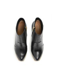 Botas de cuero negras hasta el tobillo con punteras puntiagudas, con cremalleras laterales y una textura suave; detalle de costura sutil en la parte delantera.