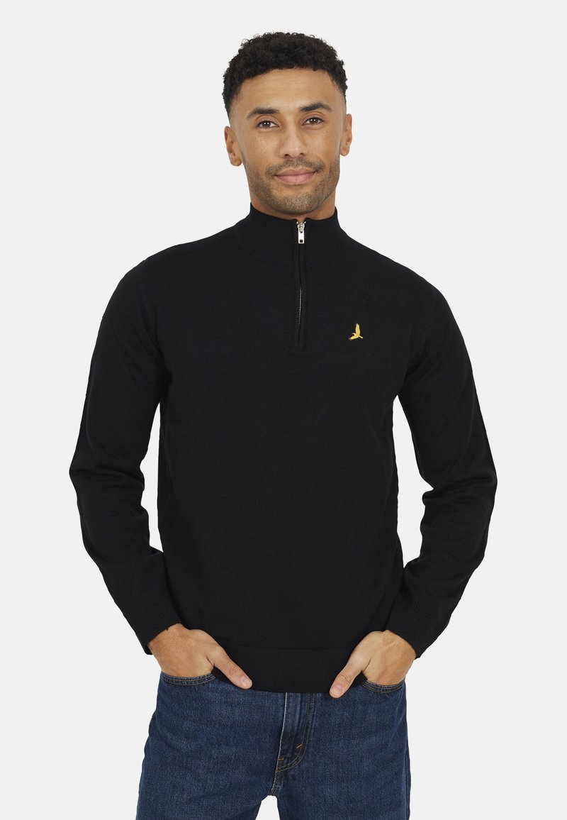 Maglione nero con zip al collo in un morbido tessuto knit. Caratterizzato da un piccolo logo di un uccellino giallo sul petto e polsini e orlo a costine. Indossato con jeans.
