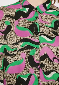 Camicia a maniche lunghe con bottoni multicolore che presenta forme astratte in rosa, verde e nero su uno sfondo fantasia color sabbia con una finitura testurizzata.