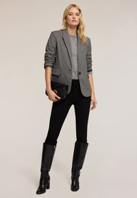 Blazer grigio di lana sopra un maglione grigio chiaro, abbinato a pantaloni neri attillati e stivali in pelle nera al ginocchio. Borsa nera con dettagli dorati.
