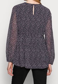 Blusa nera con un motivo floreale in rosa, dotata di maniche lunghe trasparenti, vita aderente e dettaglio a oblò sulla schiena.