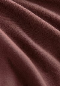 Soft, ribbed knit fabric in a deep mauve color. The material displays fine texture with subtle variations and drapes smoothly.