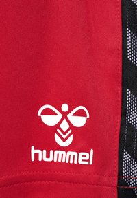 Rode stof met een gestructureerd oppervlak, voorzien van een wit Hummel-logo en een zwart geometrisch patroon aan de zijkant.