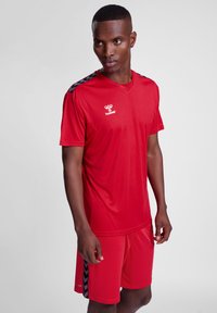 Conjunto atlético rojo que incluye una camiseta de manga corta con acentos negros y pantalones cortos a juego, fabricado con material ligero y transpirable.