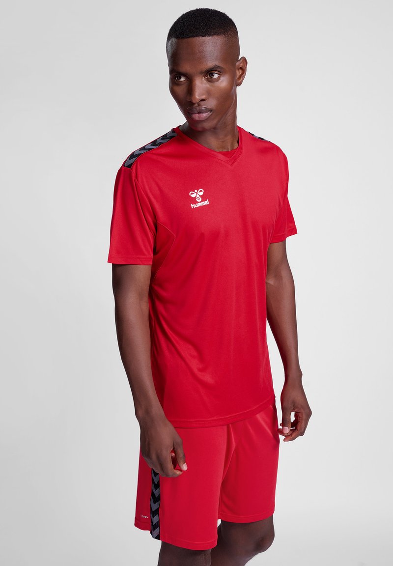Conjunto atlético rojo que incluye una camiseta de manga corta con acentos negros y pantalones cortos a juego, fabricado con material ligero y transpirable.