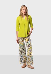 Blouse vert citron avec un col en V et des manches trois-quarts, associée à un pantalon large à motifs présentant des tourbillons de jaune, vert et gris.