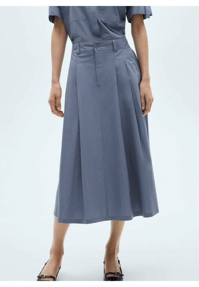 Una gonna plissettata lunga fino al ginocchio in morbido tessuto grigio, con chiusura a bottoni e tasche laterali. Scarpe nere lucide completano l'outfit.