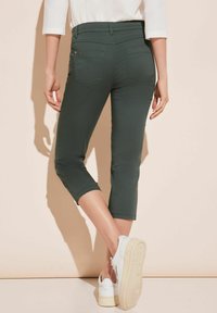 Pantalones cortos verdes con una textura suave, bolsillos traseros y un diseño ajustado, combinados con zapatillas de plataforma blancas.