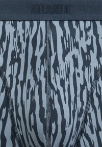 Męska bielizna z niebiesko-szarym tłem, z kontrastującym ciemnym wzorem w abstrakcyjne paski. Miękki materiał z wykończonym szwem pasem opatrzonym napisem "ATLANTIC."