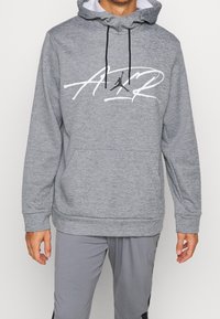 Felpa grigia con tasca a marsupio frontale, cappuccio regolabile con cordino e logo grafico bianco. Il tessuto sembra morbido con una finitura texture.