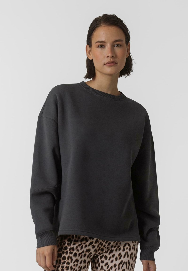 Felpa oversized grigio scuro con scollatura a girocollo, caratterizzata da maniche lunghe e polsini a costine, abbinata a leggings con stampa leopardata.