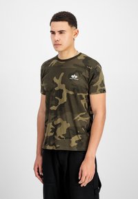 Rohelise tooni kamuflaažiprindiga T-särk, valmistatud pehmest kangast. Omab ümmargust kaelarööpamatut ja logo plaastrit vasakul rinnaku piirkonnas.