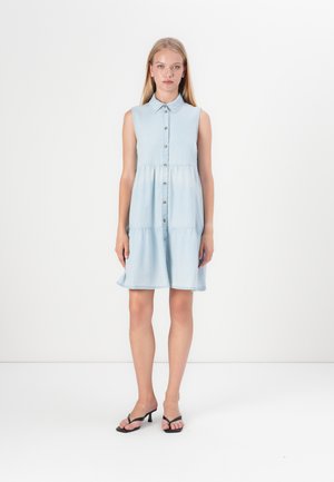 Light blue denim sleeveless dress with a collar, button front, and gathered waist. Flared skirt ends above the knee. Worn with black sandals.