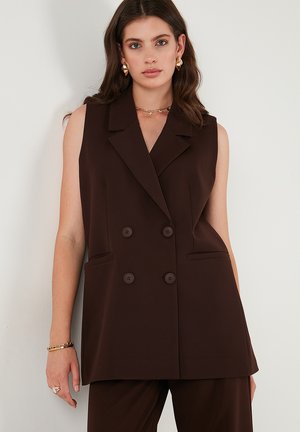 Brown sleeveless blazer with a double-breasted front, notch lapels, two side pockets, and large buttons. Smooth fabric with a structured fit.