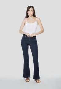Donkerblauwe denim flared jeans met hoge taille en een strakke witte tanktop. Sandalen met bandjes. Eenvoudige, gladde textuur.
