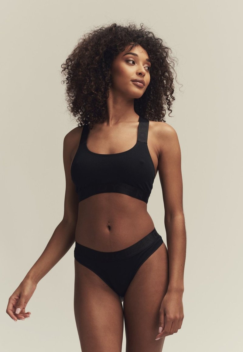 Zwarte sportbh met brede banden en bijpassende hoogrisque bikini-onderdelen. Glad materiaal met subtiele branding op de band. Platte naden.