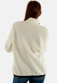 Maglione in pile avorio con colletto alto, superficie texturizzata e orlo blu navy arricciato. Presenta una vestibilità ampia e senza chiusure visibili.