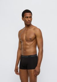 Μαύρα βαμβακερά μποξεράκια με εφαρμοστή σχεδίαση. Διαθέτουν ελαστική μέση με λογότυπο. Λεία υφή και μήκος μέχρι το μέσο του μηρού.