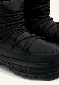 Crne izolirane čizme napravljene od najlona i gume, s podstavljenim gornjim dijelom, sintetičkim vezicama i teksturiranim, robusnim potplatom za bolju prionjivost.