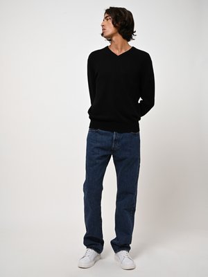 Suéter negro de cuello en V, con textura trenzada, combinado con jeans de azul oscuro y zapatillas blancas. Diseño sencillo, corte relajado, con hardware mínimo.