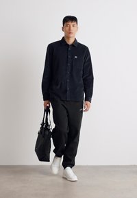Zwarte corduroy knoopshirt met een borstzak, zwarte sweatpants, witte sneakers en een zwarte tote bag. Minimalistisch ontwerp, casual fit.