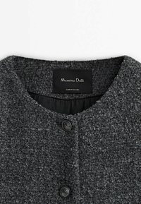 Manteau en laine texturée gris foncé, col rond, deux boutons noirs et une étiquette noire mentionnant Massimo Dutti fabriqué en Roumanie.