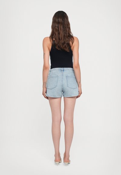Shorts en denim bleu clair, avec une taille haute, deux poches arrière et un ourlet retroussé. Assortis à un top noir ajusté.