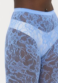 Leggings blu in pizzo con un motivo floreale, texture trasparente, vita elastica e design aderente.